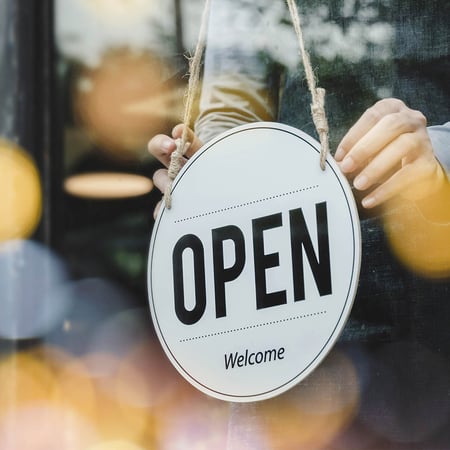 A person hangs an open sign in a storefront window