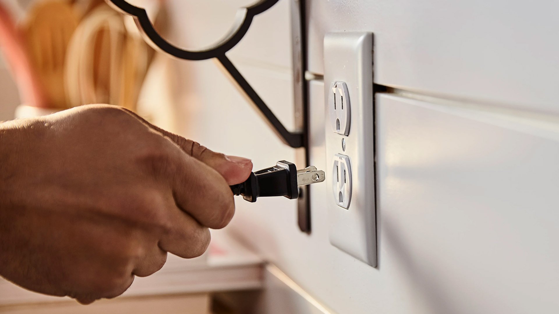 Close up shot of a hand plugging in a cord to a wall outlet.