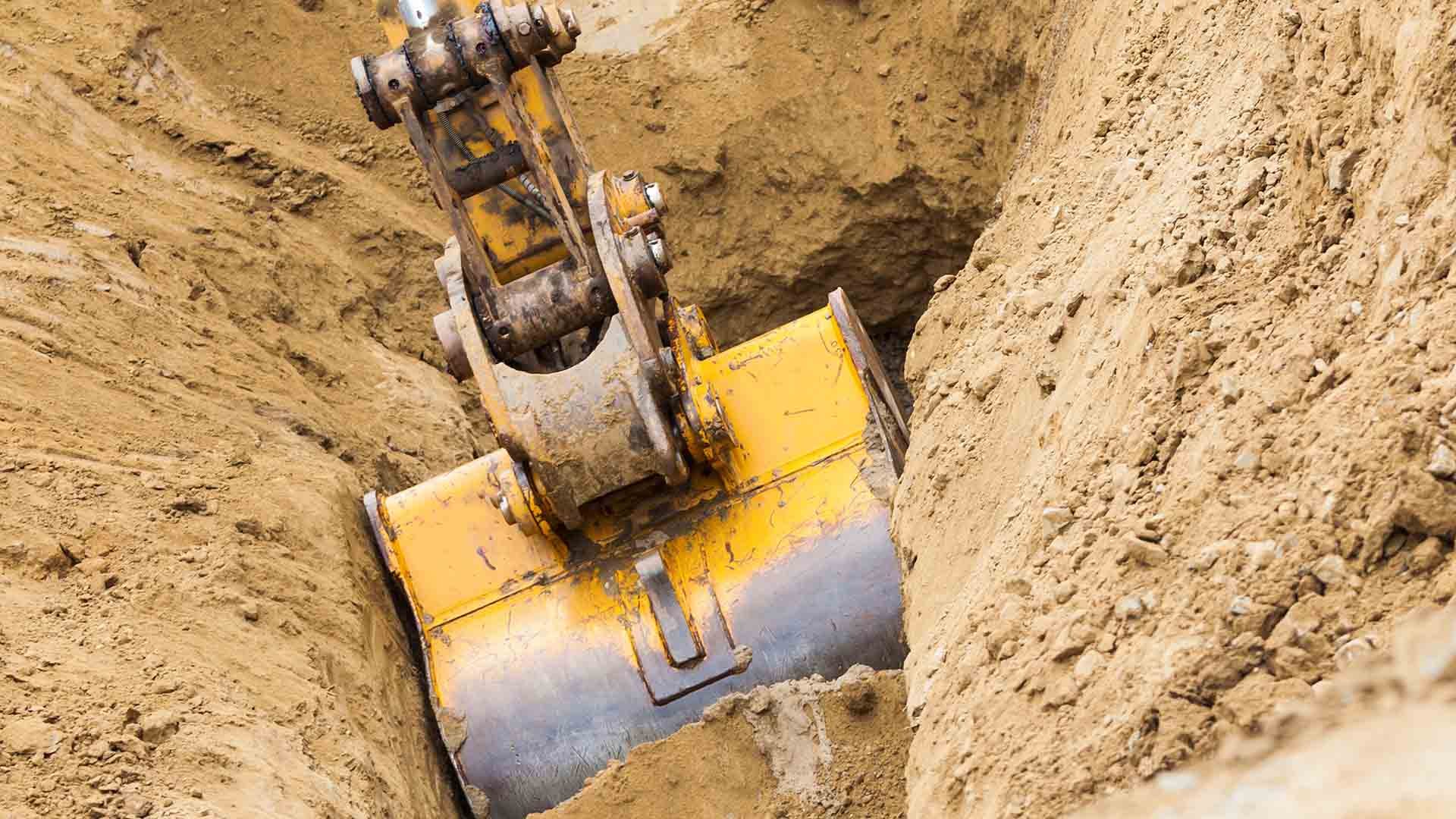 A yellow bucket of an excavator scoops soil.