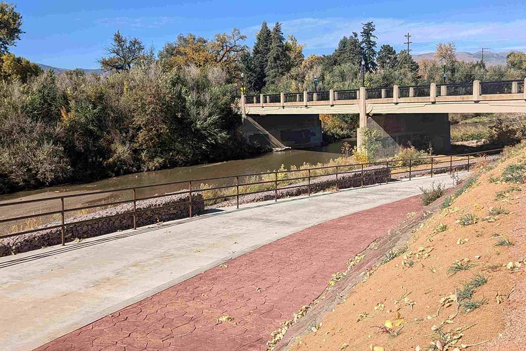 A recently constructed walkway runs parallel to Monument Creek on a sunny day. 