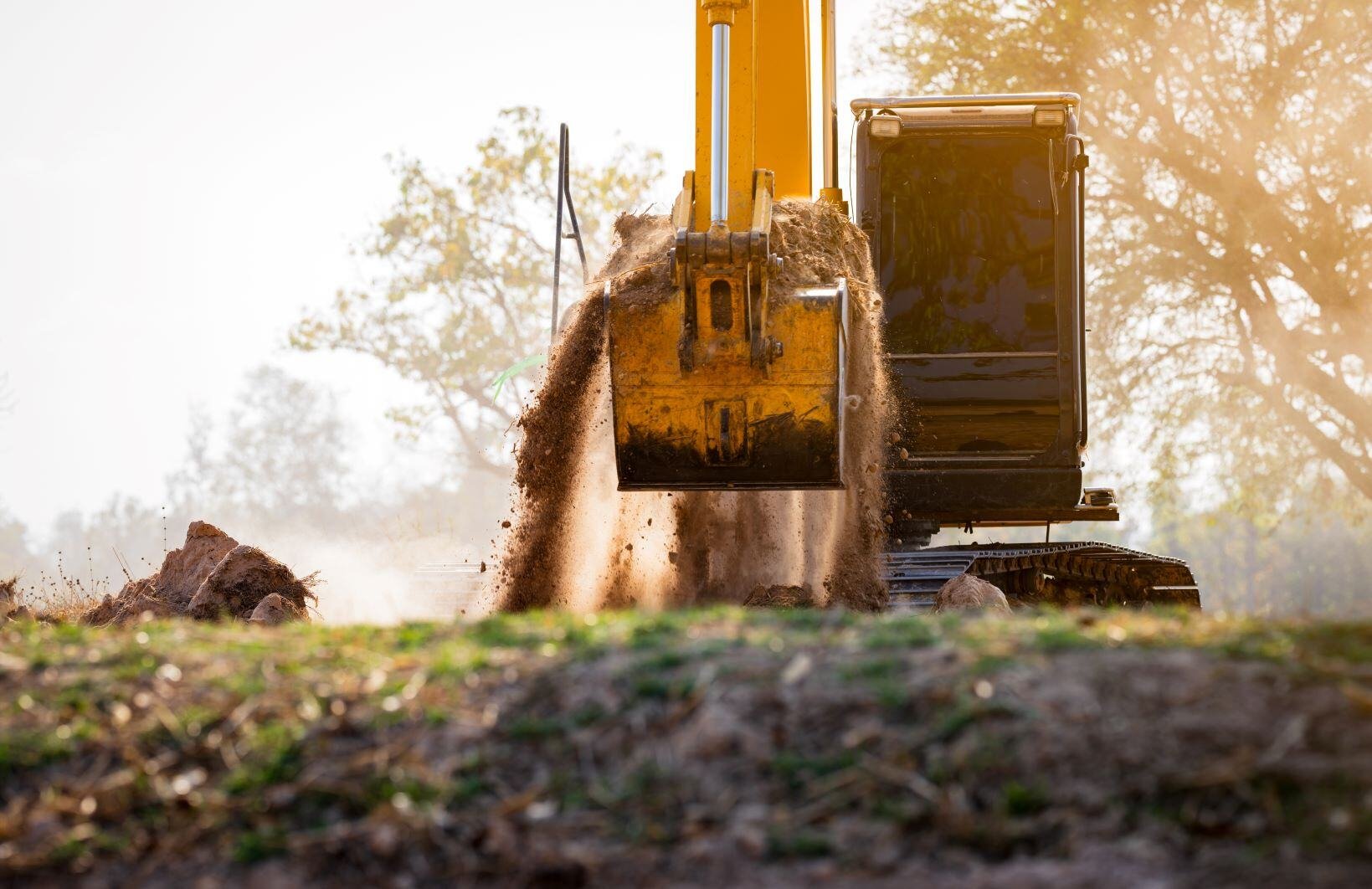 An excavator digging into the ground with dirt overflowing out of the bucket.