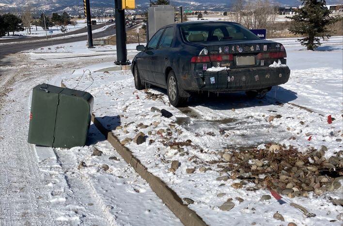 A black Toyota car sits on the side of a snow covered road near an intersection after hitting a small residential transformer. 