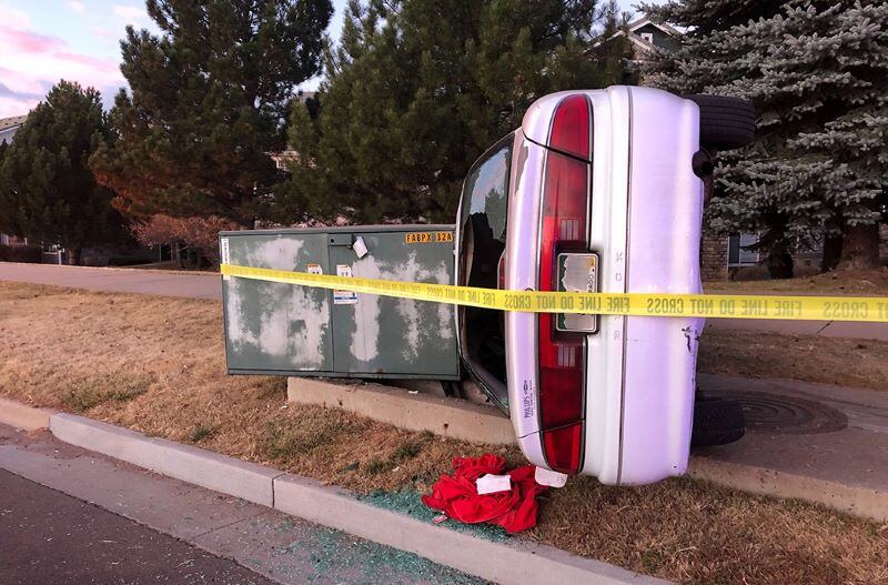 A car lies on its side, leaning against a large residential transformer that's been partially disconnected from the ground. The car is white and pink.