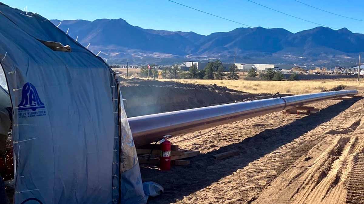 A grey gas pipeline stretches across a dirt field with Rampart Range visible in the distance in Colorado Springs.