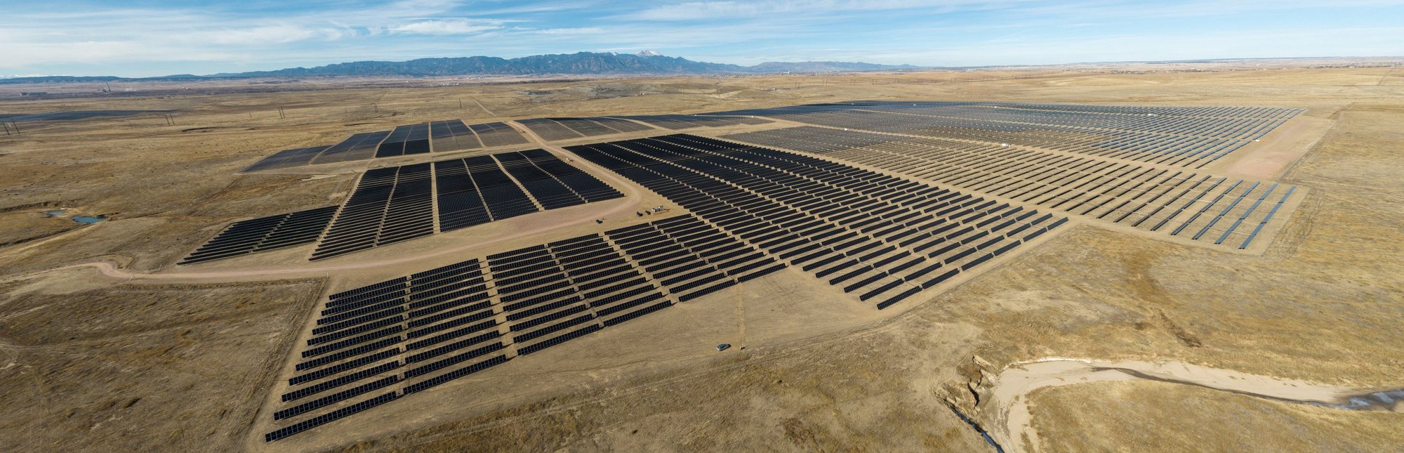 Aerial view of the vast Pike Solar Array. Rows of solar panels spread across a dry, flat landscape, with mountains in the distant background.