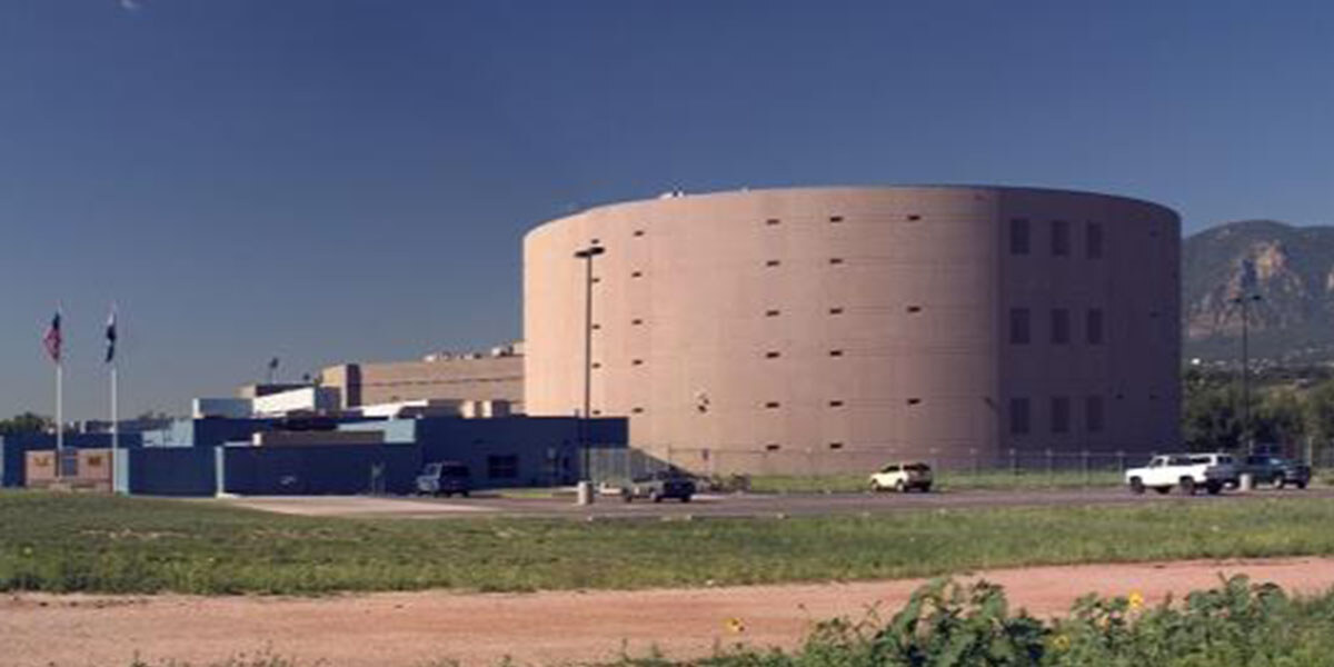 A large brown water treatment tank. A blue building is attached to the tank with a few cards parked in front. 