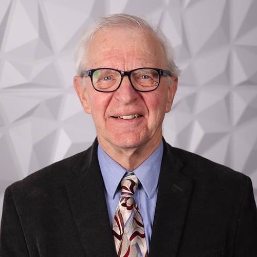 A photograph of a man wearing glasses named Larry Barrett. He is standing in front of a white textured background and is wearing a black suit.