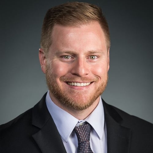 Photo portrait of UPAC member Michael Borden. He is wearing a black suit with a grey undershirt and maroon and blue patterned tie. 