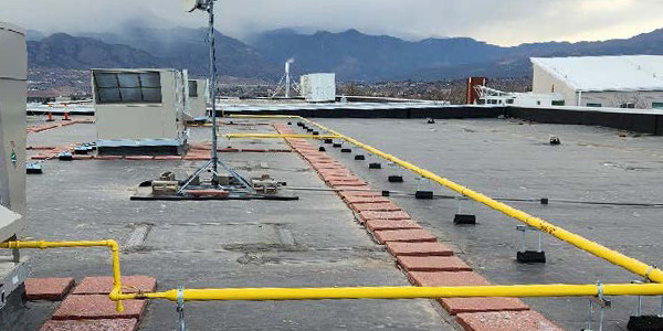 Photo of a rooftop in Colorado Springs on a cloudy day. Swamp cooler units line the top of the building, with yellow pipes running along the roof.