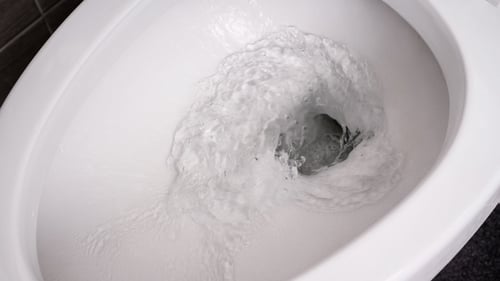 A close up photograph of a toilet flushing clear water. 