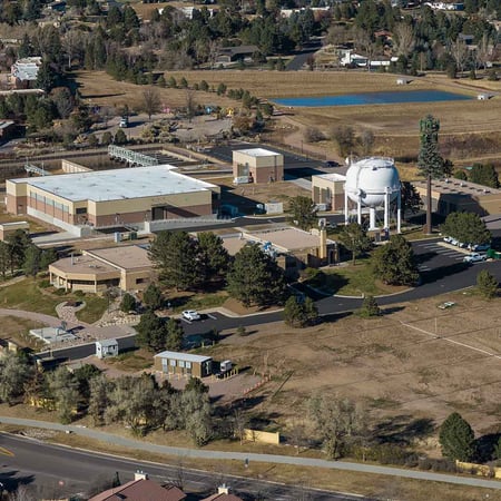 Aerial photo of Tollefson water treatment plant. Two large brick buildings, parking lots, cars, a white water tower, & 2 ponds make up the footprint.