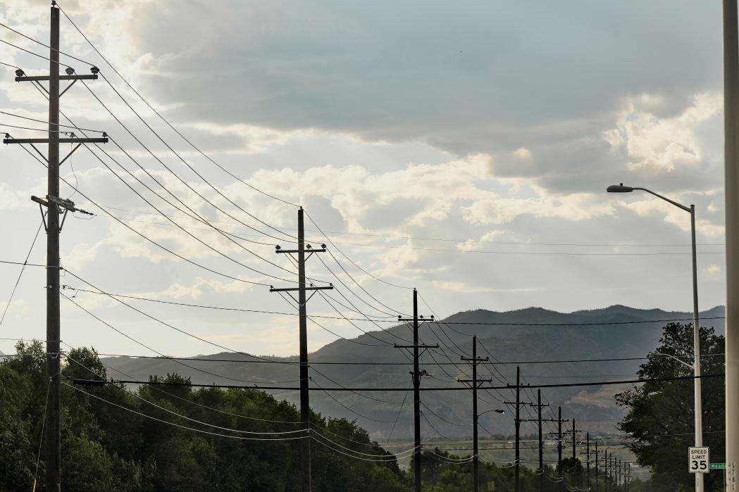 A line of utility poles and electric lines along a street in Colorado Springs. Mountains are visible in the background. It's a mostly cloudy day.