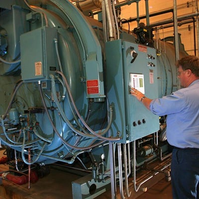 A person pressing buttons on the panel of a large, blue piece of industrial equipment.