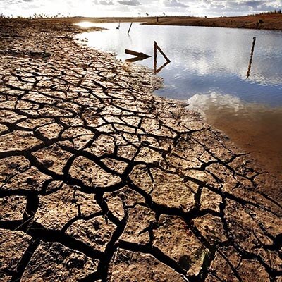 A small body of water surrounded by dry and cracked ground. The day is sunny, indicating heat and dry conditions.