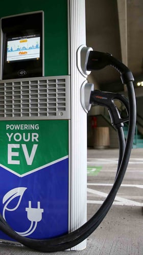 An EV charging station in a parking garage. The front of the station has a decal sticker that reads "POWERING YOUR EV"