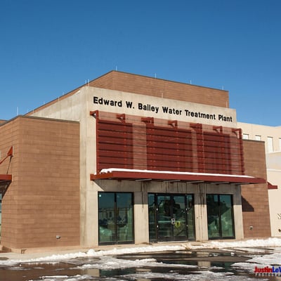 Building name: "Edward W. Bailey Water Treatment Plant." There are glass doors and a red awning on a tan brick building with melted snow outside.