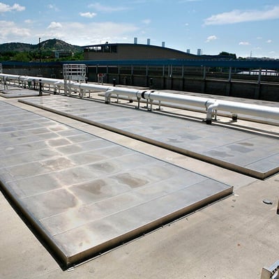 The JD Phillips Water Resource Recovery Facility on a sunny day. A white pipe is visible and there are covered basins visible in the foreground.