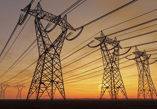 Multiple high-voltage power lines and towers silhouetted against a vibrant sunset. 