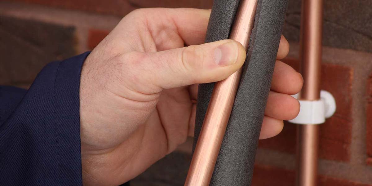 A close up shot of a hand covering a copper pipe with insulation. 