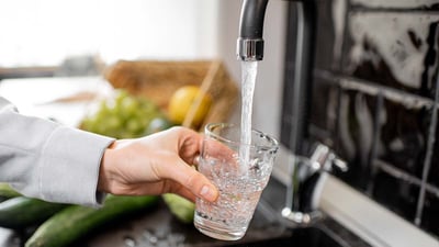 A hand using a faucet to fill a cup with water.