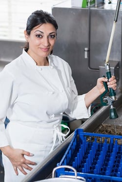 A person wearing a chef's uniform in a commercial kitchen with her hand on a water sense pre-rinse spray nozzle at a sink.