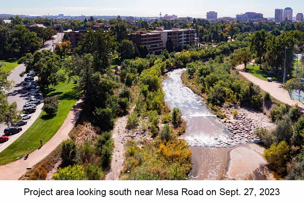 Aerial photo of Monument Creek taken on September 27, 2023. The creek meanders through a green landscape. The city skyline is also visible.