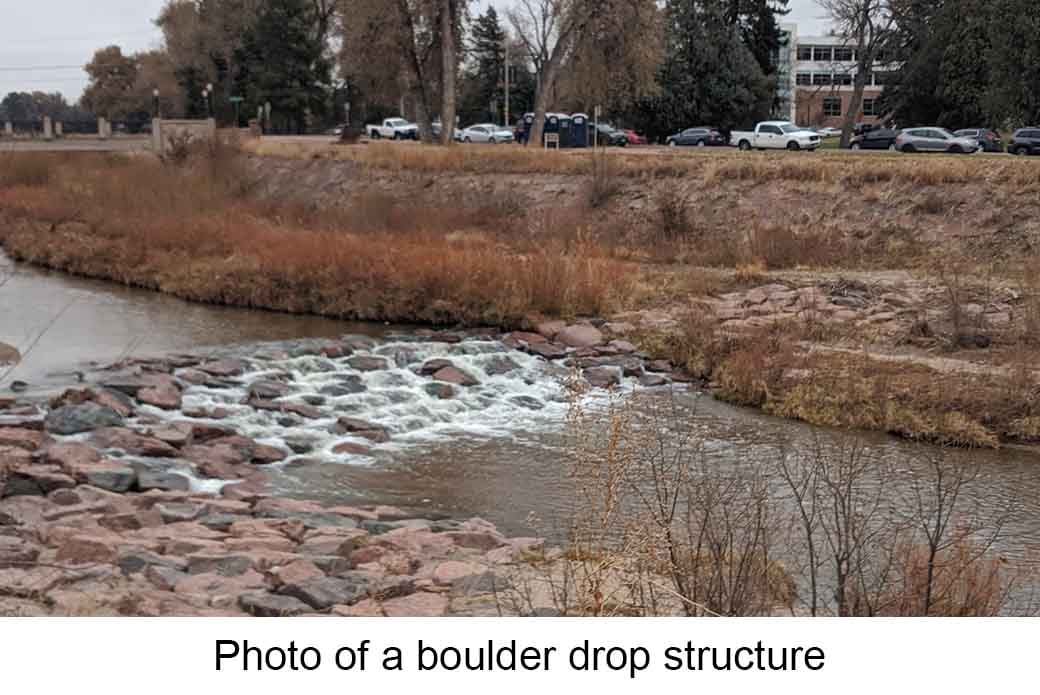 A "boulder drop structure" in a river setting. A series of large, flat rocks placed across a river creating small cascades of water. 