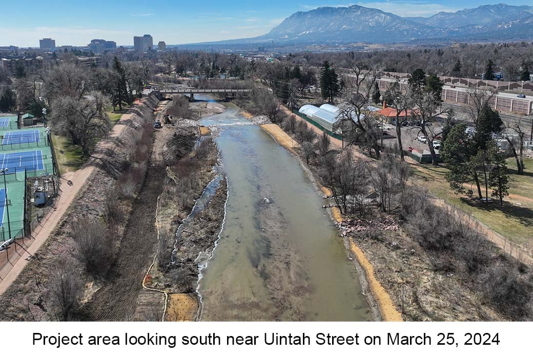 Aerial photo of Monument Creek taken on March 25, 2024. Water rushes over boulders in the creek in the distance. Some boulders are visible on the bank