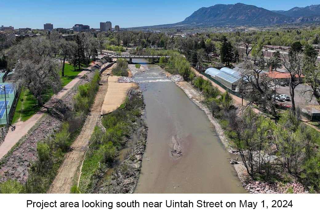 Aerial photo of Monument Creek taken on May 1, 2023. Water rushes over boulders in the distance. Yellow straw is on the bank of the creek nearby.