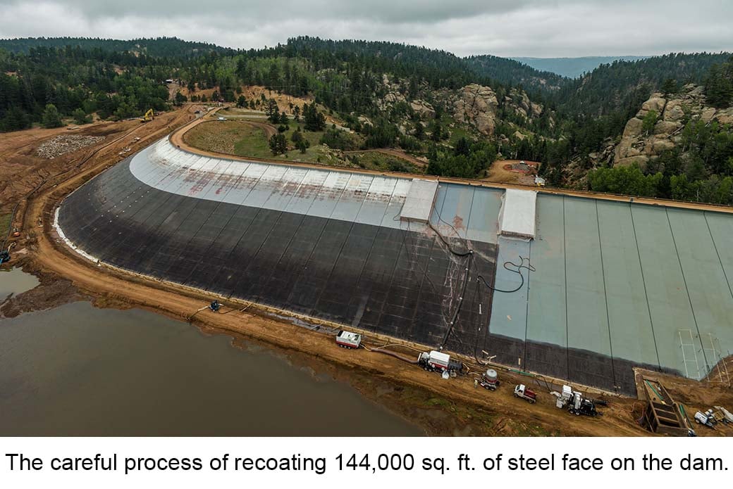 Work continues on the South Catamount Dam. A portion of the dam is dark grey, showing the progress of the crews resurfacing the dam. A caption on the image reads "The careful process of recoating 144,000 sq. ft. of steel face on the dam.."