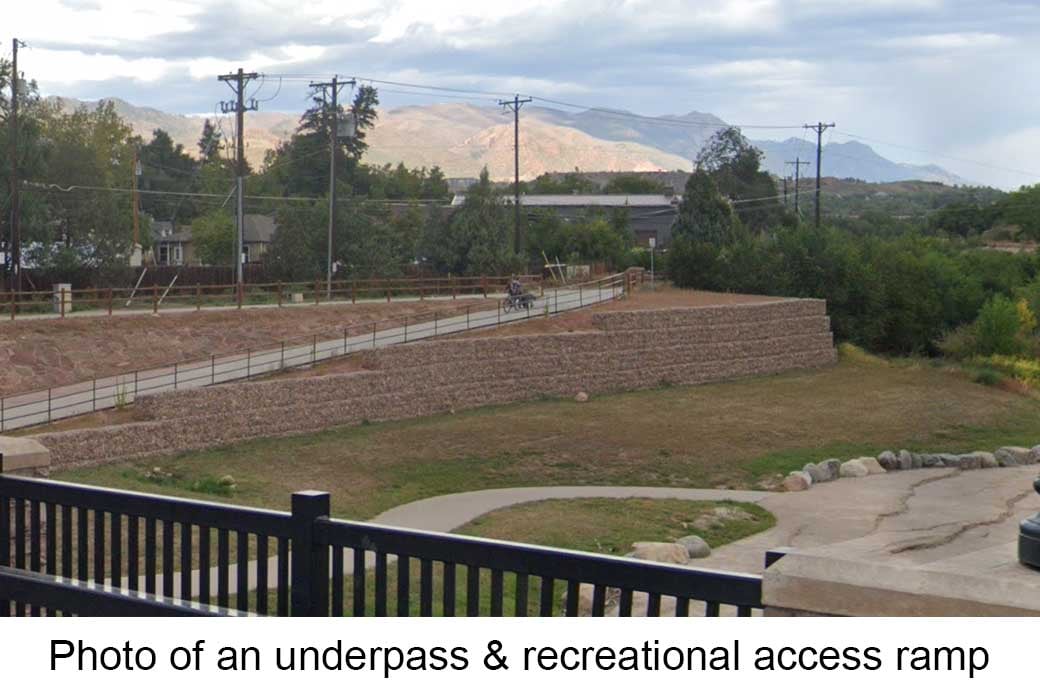 An underpass with a pedestrian access ramp. The underpass is constructed with a block wall and there are metal railings along the edge of the ramp.