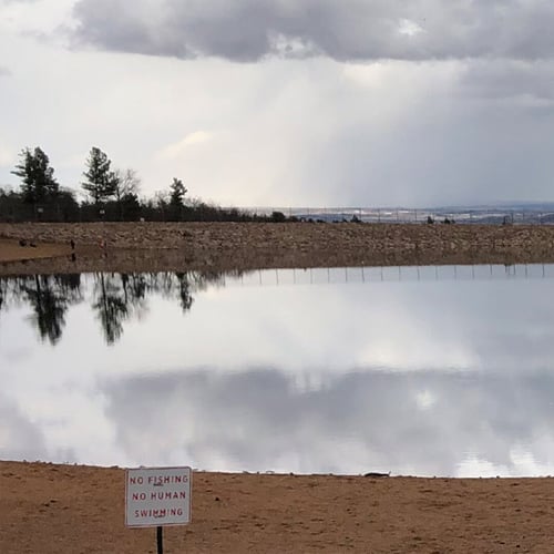 Body of water with a rocky shore visible in the distance on a cloudy day. A sign on the shore reads "No fishing, no human swimming"