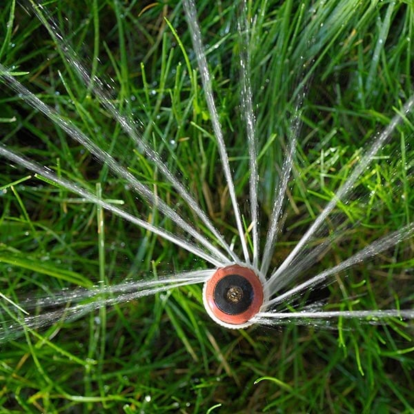 A sprinkler spraying approximately 10 concentrated streams of water on to green grass.